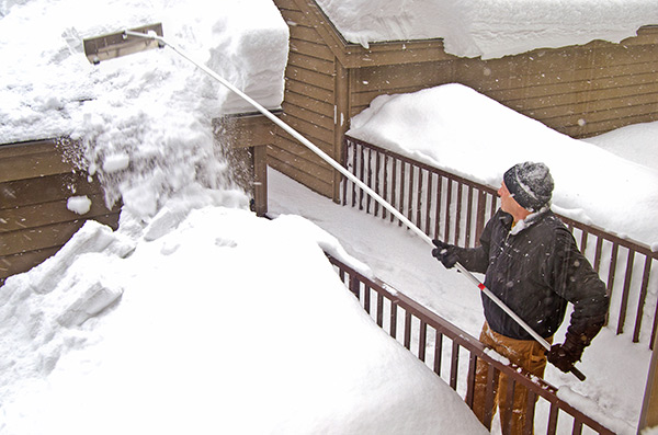 Man removing snow from a roof with a roof rake