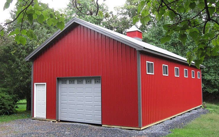 Crimson red pole barn workshop with a white roof, a large white door, and a small white door