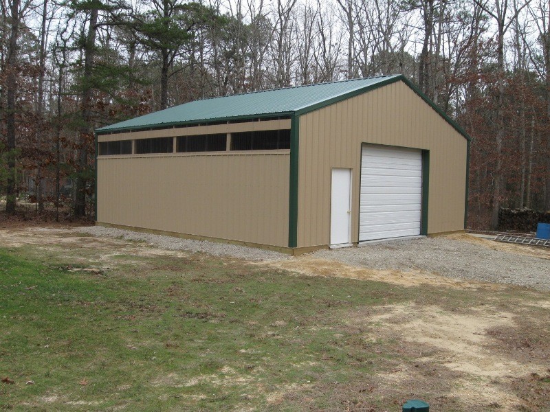 Tan pole barn garage with an evergreen roof, a large white door, and a small white door